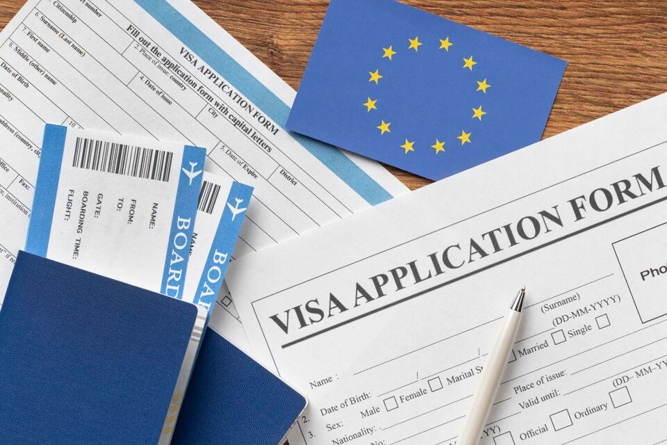 A Schengen visa application form on a wooden desk with an EU flag, a passport and boarding passes laid across it.